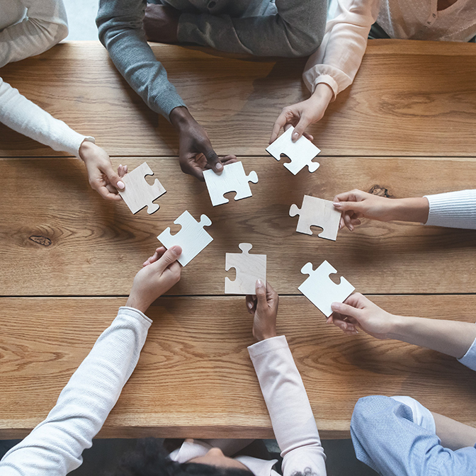 hands reaching across a table to put a puzzle together